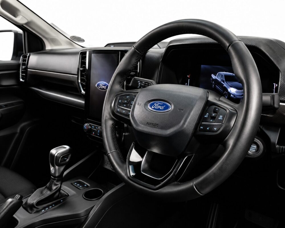Interior of a Ford vehicle showing the steering wheel with logo, center console, and large display screens on either side.