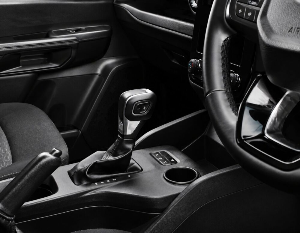 Close-up of a car's center console featuring an electronic gear shifter with a plus/minus control, cup holder nearby.