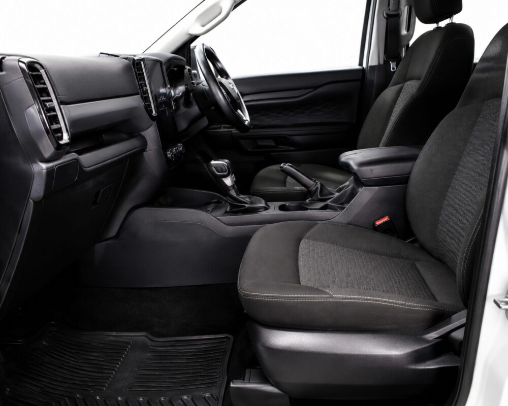Front interior of a car: black fabric seats, steering wheel, and center console with gear shifter visible by the driver’s seat side.