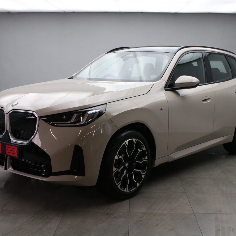 Beige BMW SUV in a studio, shown from a front three-quarter angle with a prominent kidney grille and black alloy wheels.