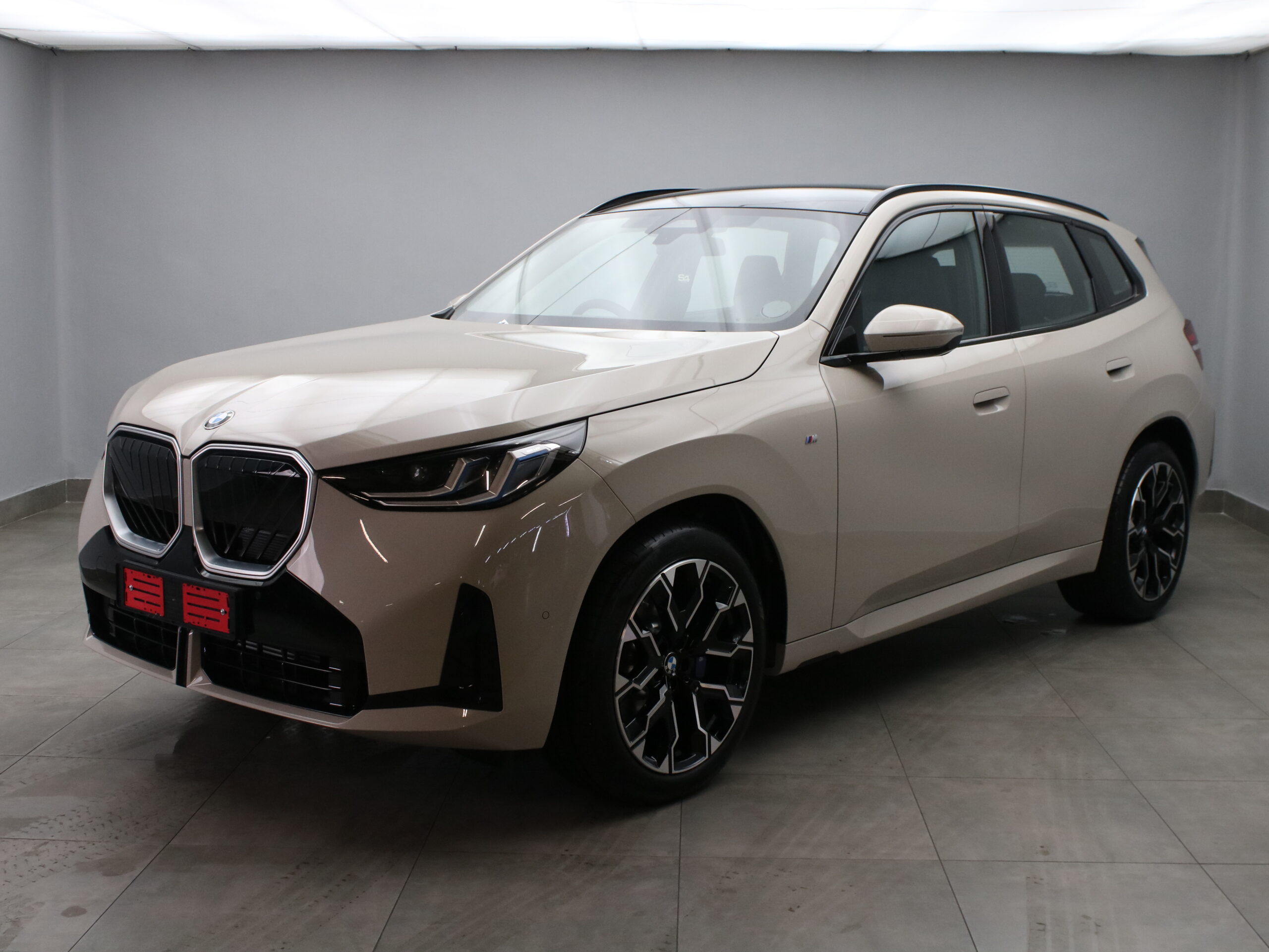 Beige BMW SUV in a studio, shown from a front three-quarter angle with a prominent kidney grille and black alloy wheels.