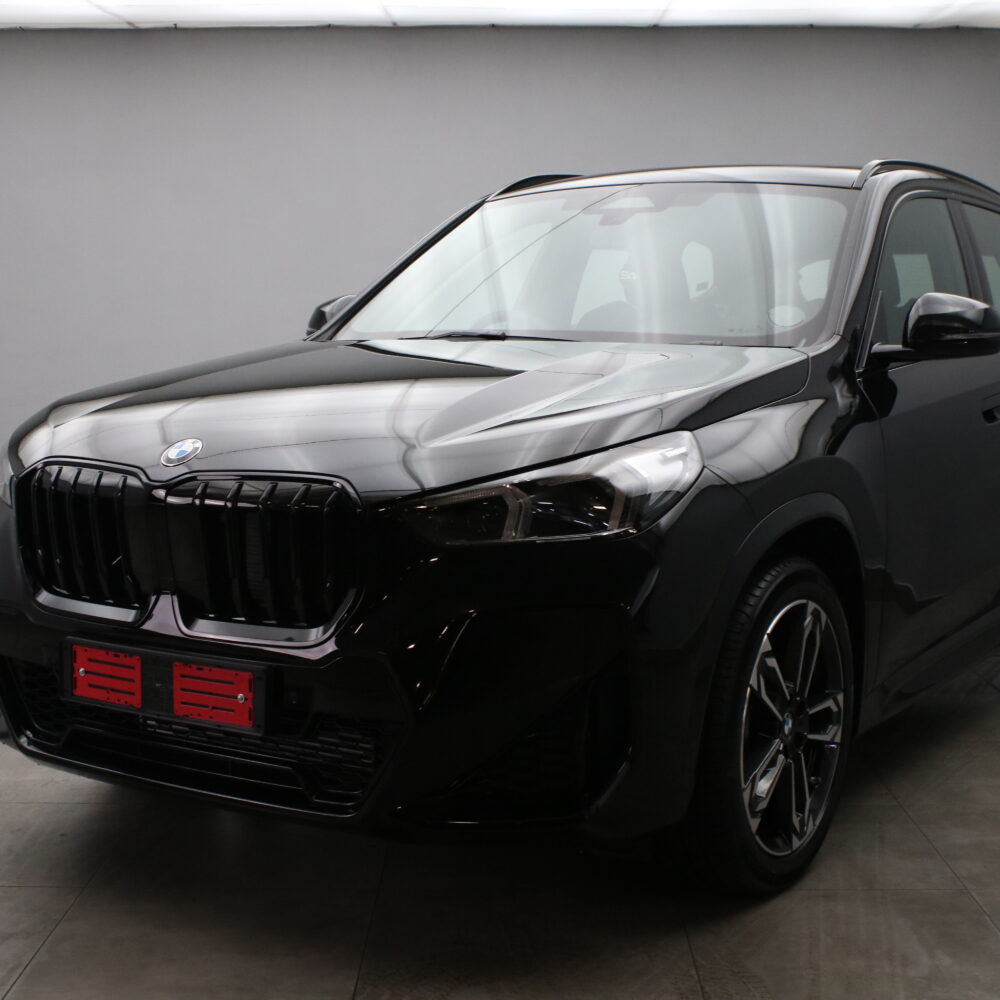 Black BMW crossover SUV in a showroom, front-left angle showing the glossy finish and distinctive kidney grille.