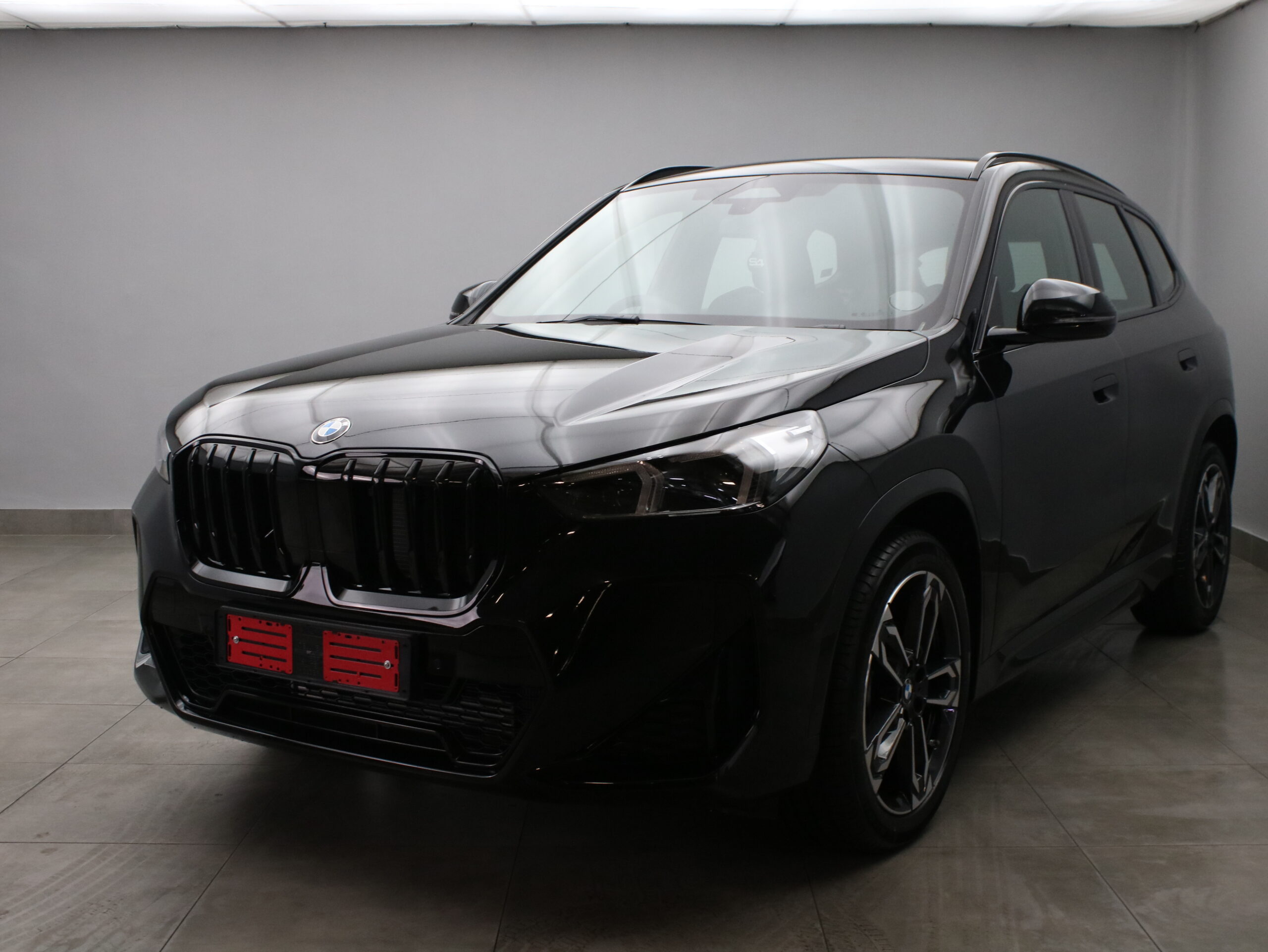 Black BMW crossover SUV in a showroom, front-left angle showing the glossy finish and distinctive kidney grille.