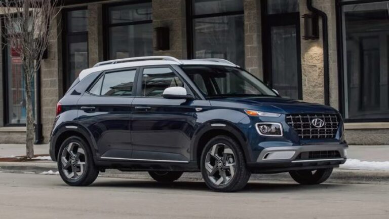 Blue SUV with silver roof rails parked on a city street in front of a stone storefronts and large windows.
