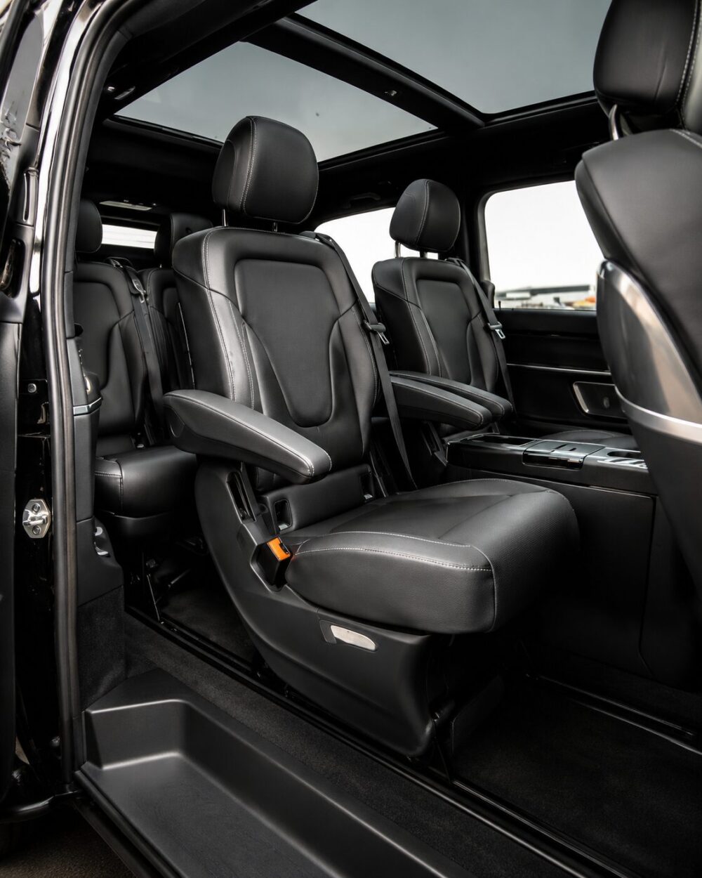 Black leather SUV interior with two captain seats and a panoramic sunroof, seen from the open rear door edge.