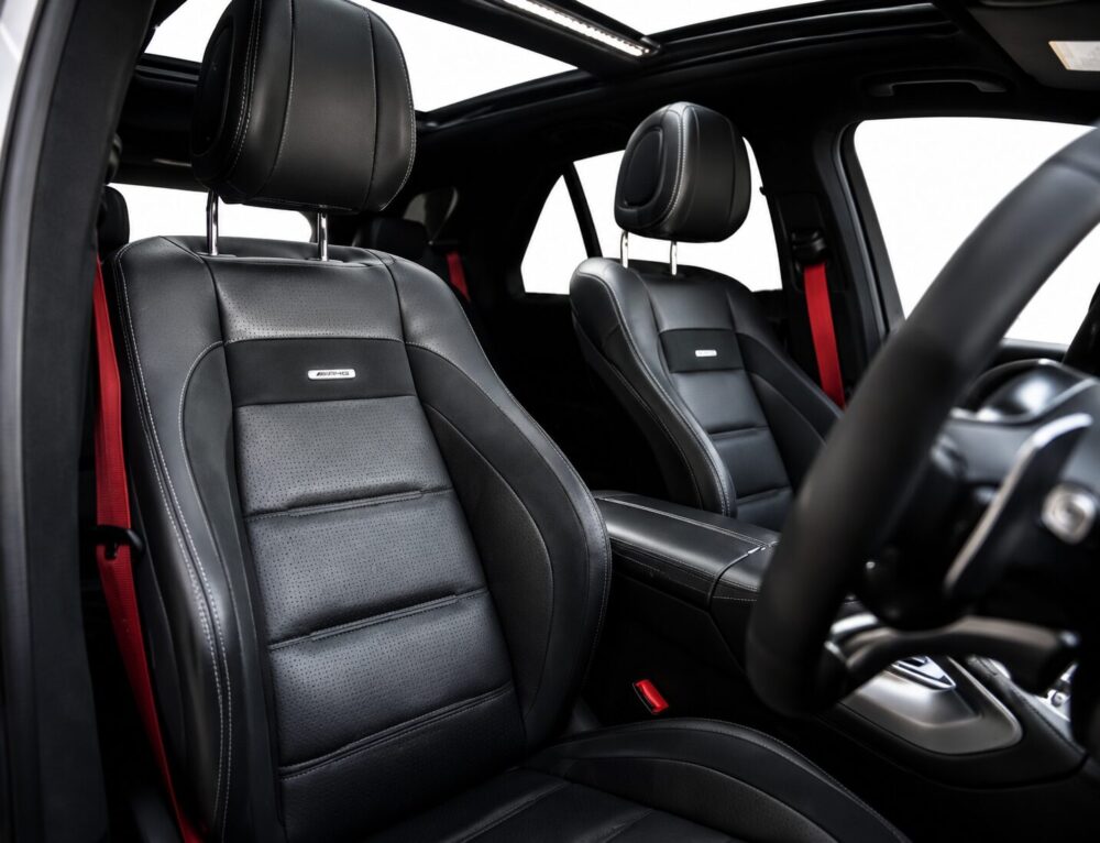Luxurious black leather car seats with white stitching, front interior of a modern SUV, illuminated cabin and red seat belts