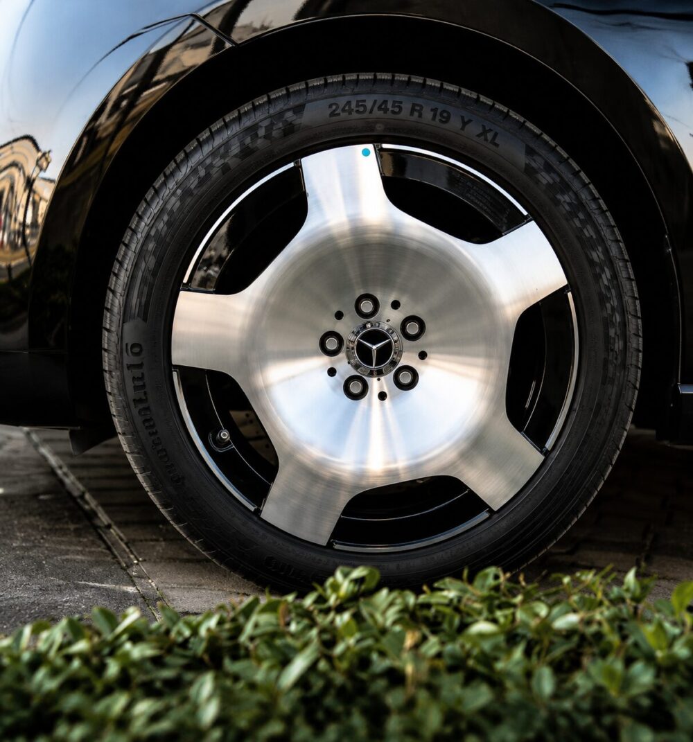 Close-up of a shiny Mercedes alloy wheel and tire on a black car, with a blue valve cap and a reflective, brushed-metal center.