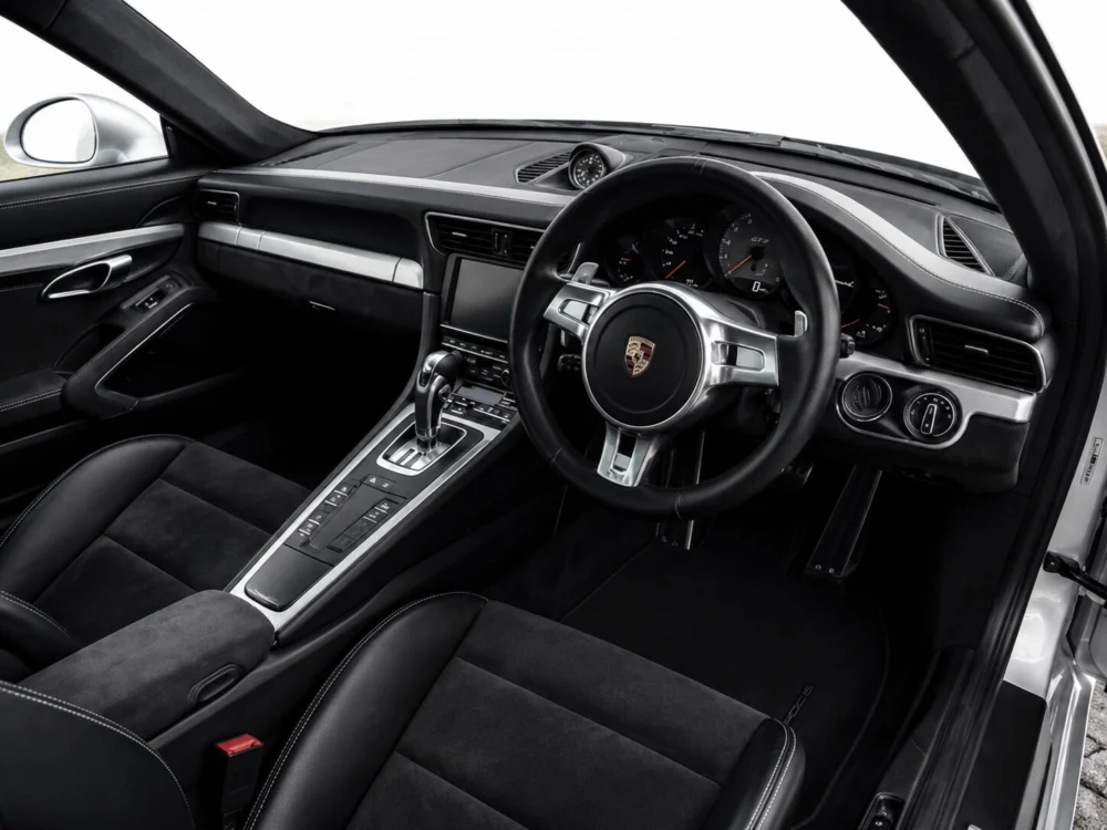 Luxurious black car interior featuring a Porsche steering wheel, center console, and instrument cluster viewed from the passenger side.