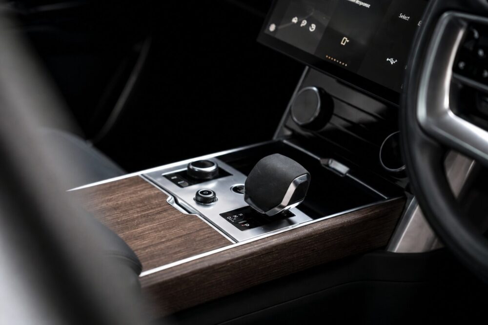 Modern car interior: close-up of the gear selector on a woodgrain center console with metallic trim.