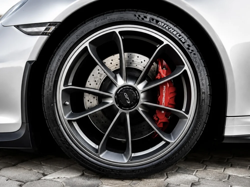 Close-up of a Porsche alloy wheel with a drilled brake rotor and red brake caliper behind the spokes.