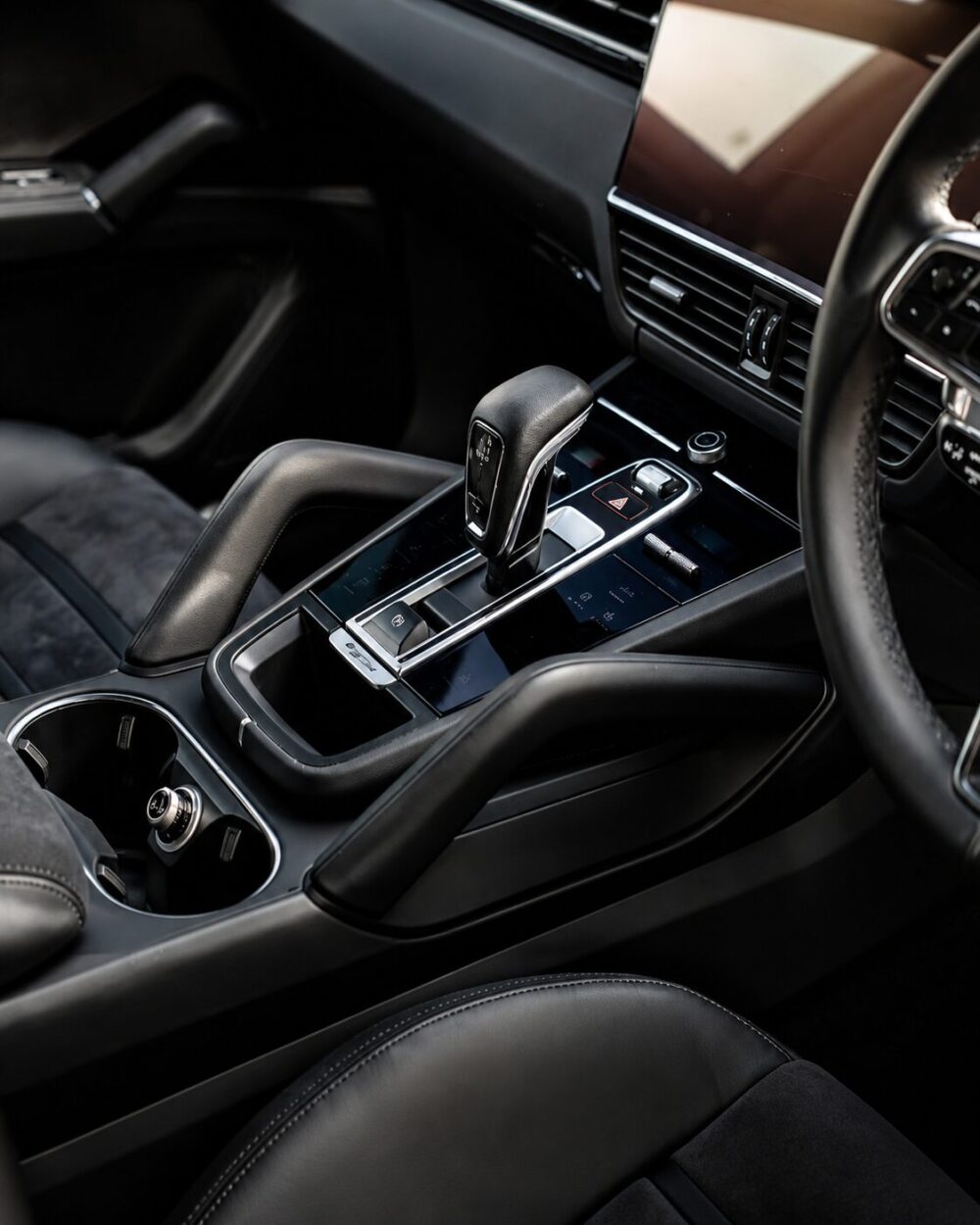Center console of a dark leather car interior with the automatic gear shifter, cup holder, and glossy trim panels nearby